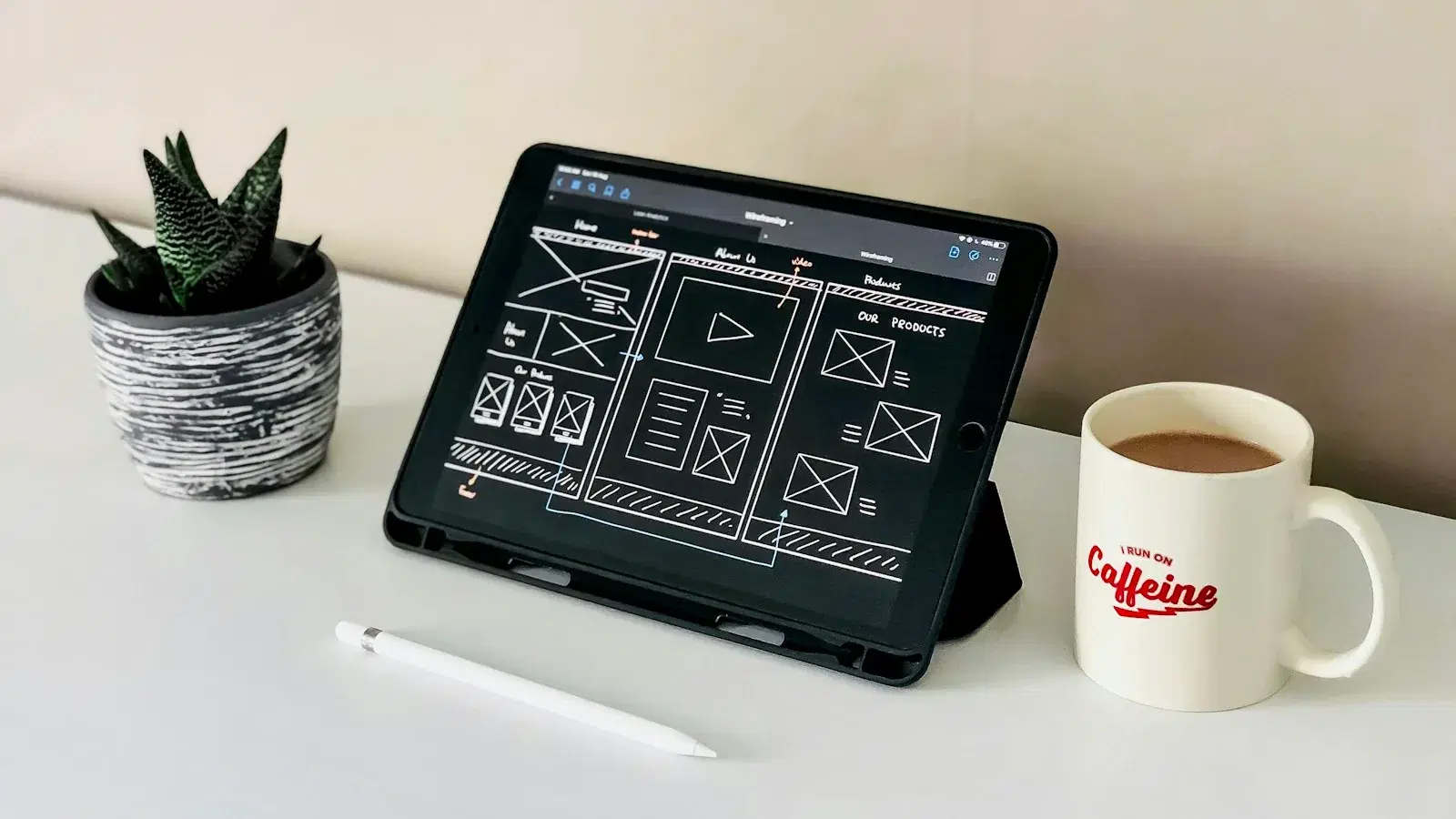 A tablet showing a user-interface wireframe sketch on a desk beside a mug.