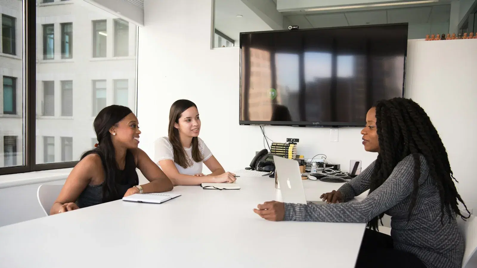 Three colleagues talking across a table in a meeting room.