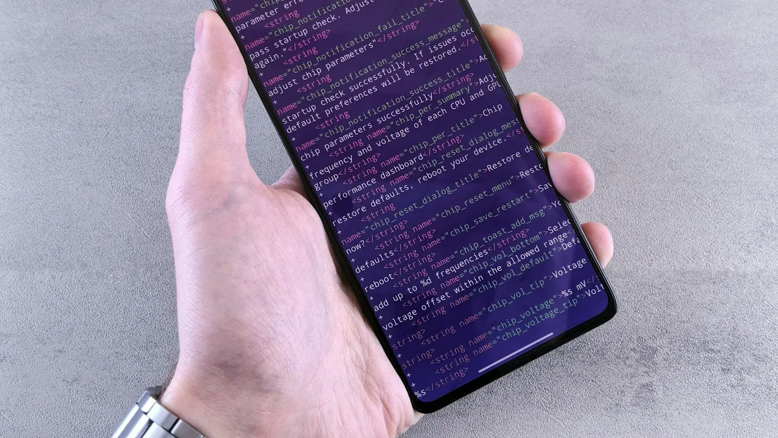 A hand holding a phone whose screen is filled with lines of code.