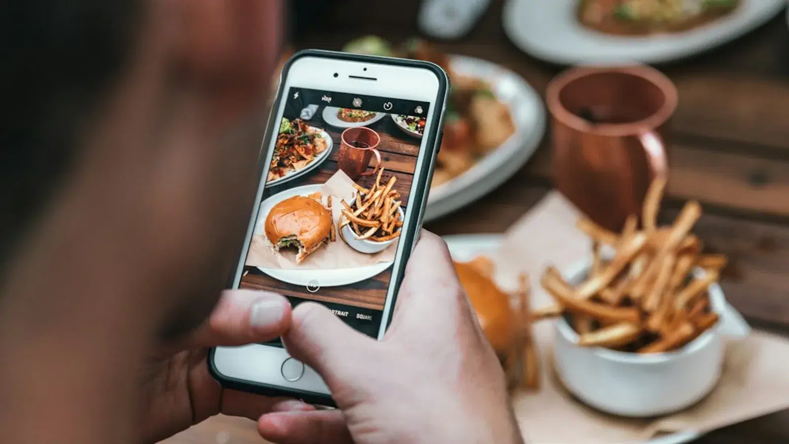 Someone photographing a burger and fries on a phone at a restaurant table.