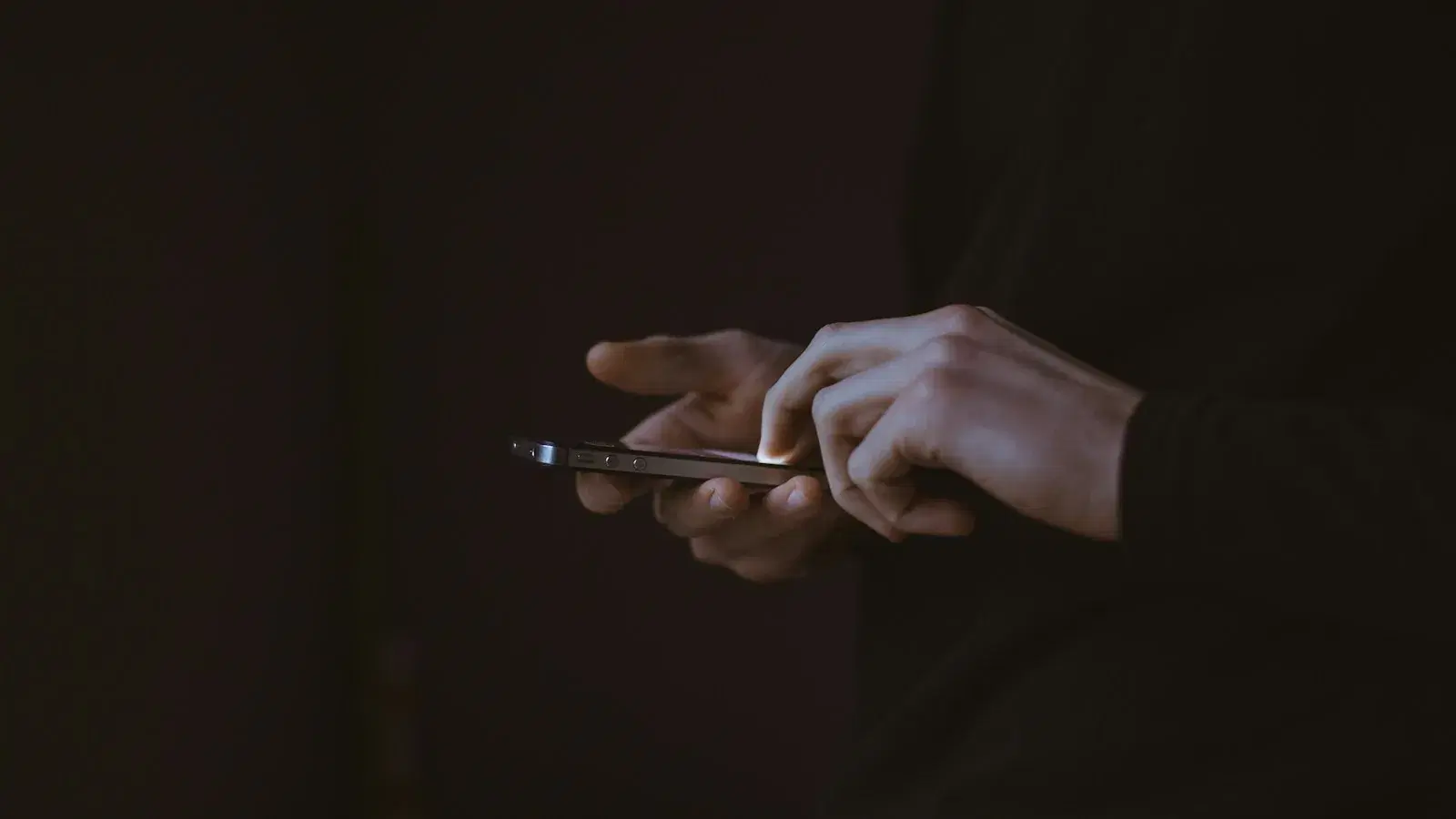 A pair of hands using a phone in near darkness, the screen the only light.