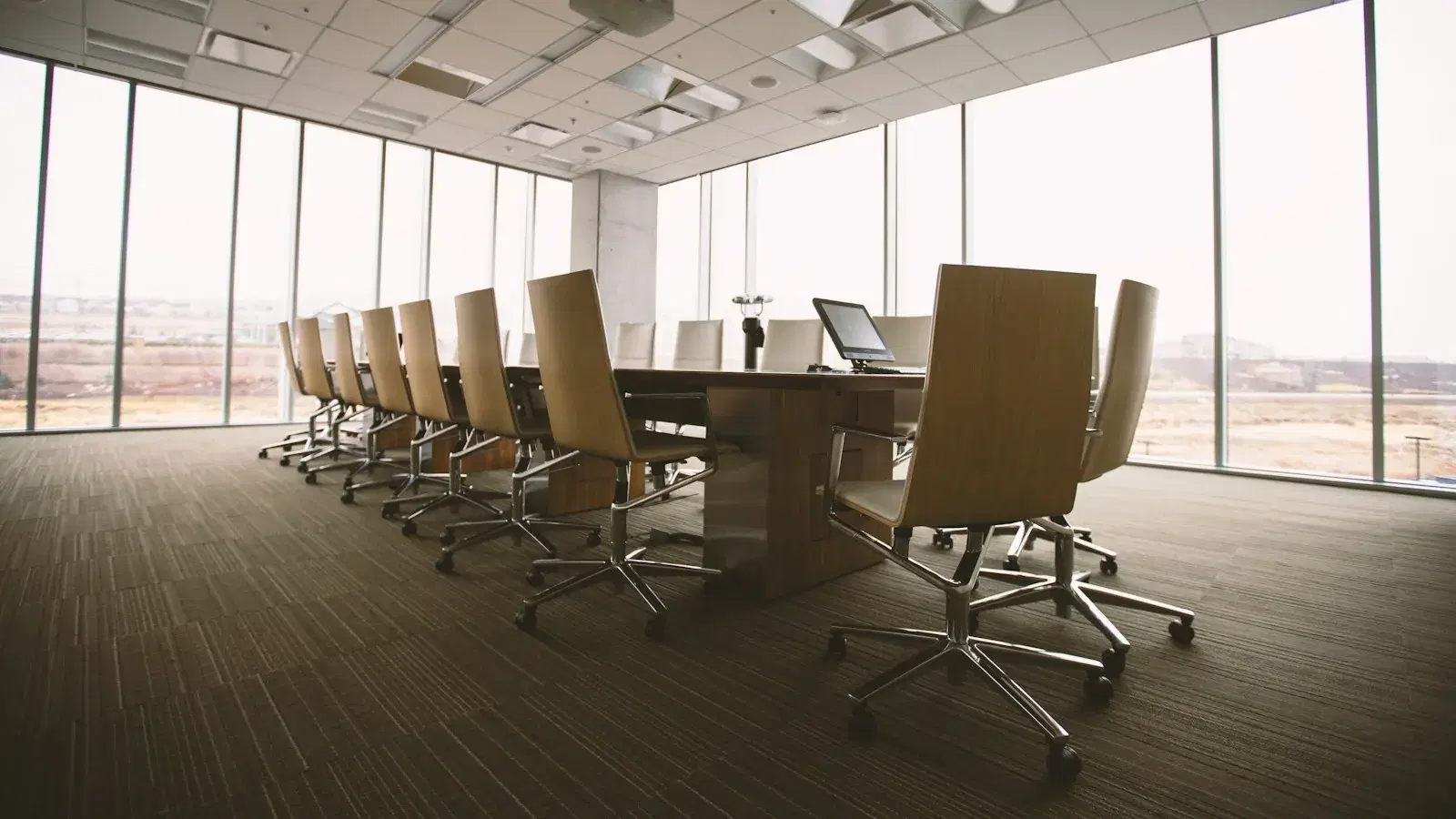 An empty boardroom with a long table and chairs beside floor-to-ceiling windows.