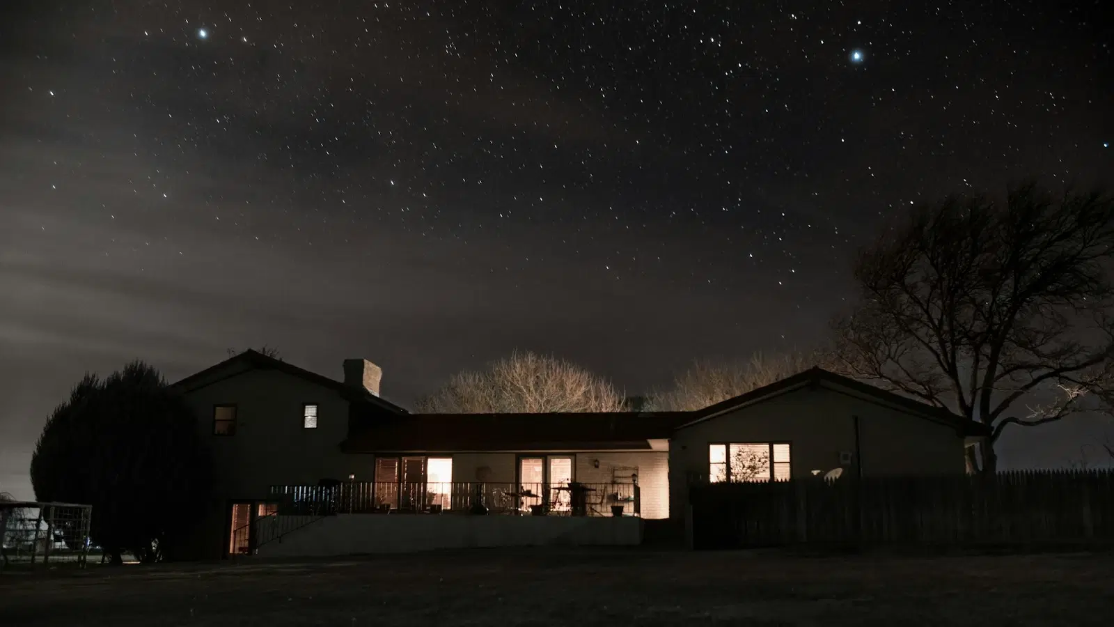 A single house lit from within, photographed at night under a wide dark sky.