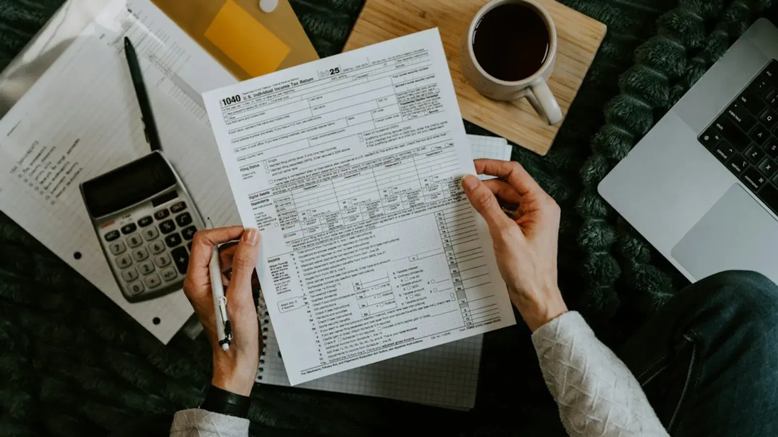 Hands holding tax forms with calculator and laptop