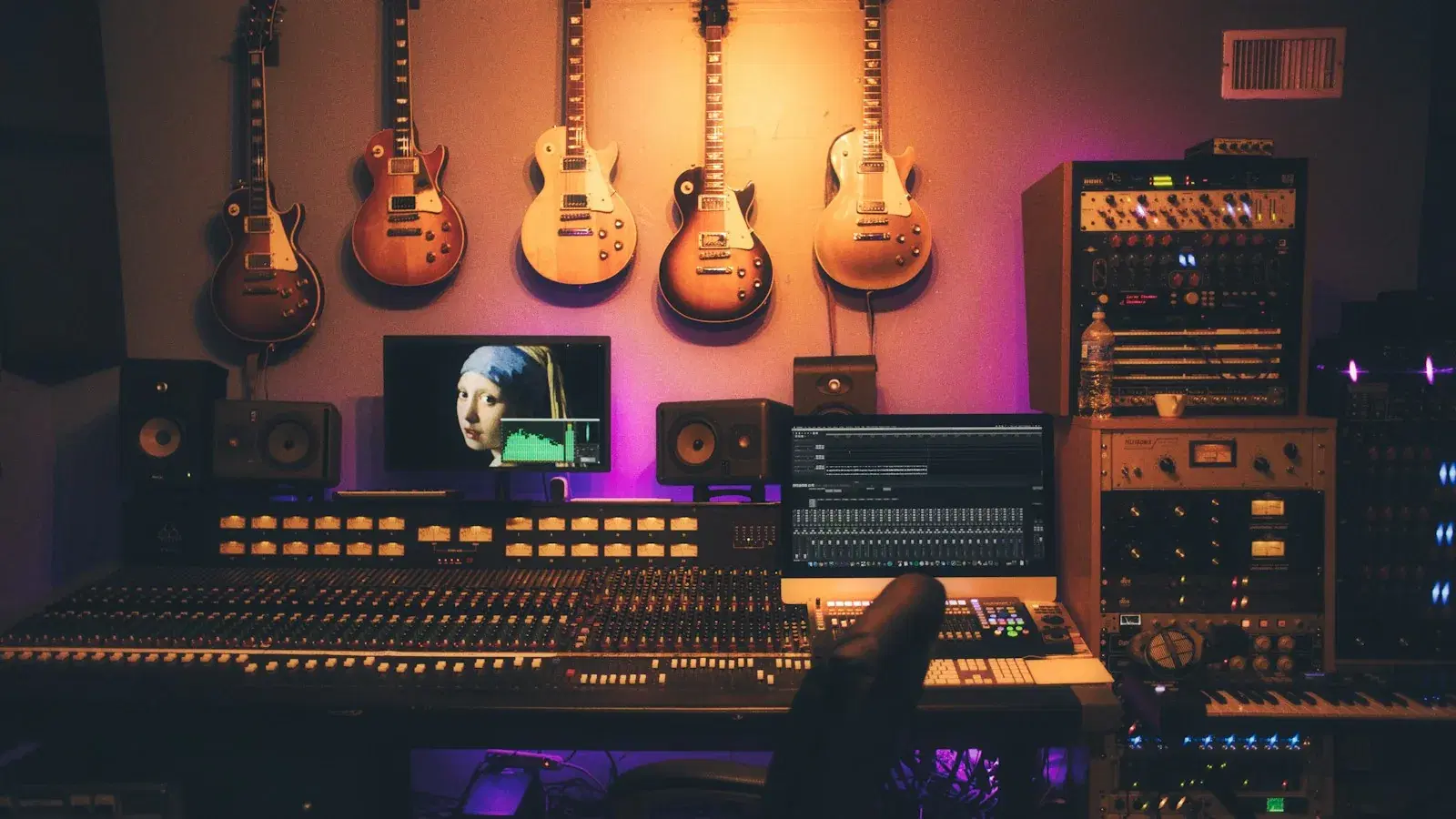 A recording studio with guitars on stands beside a large analogue mixing console.