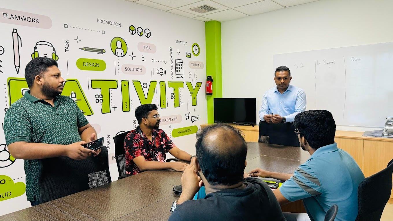 Five members of the iLeaf team in a stand-up around the table in the Kochi office, with a To Do / In Progress / Done board behind them
