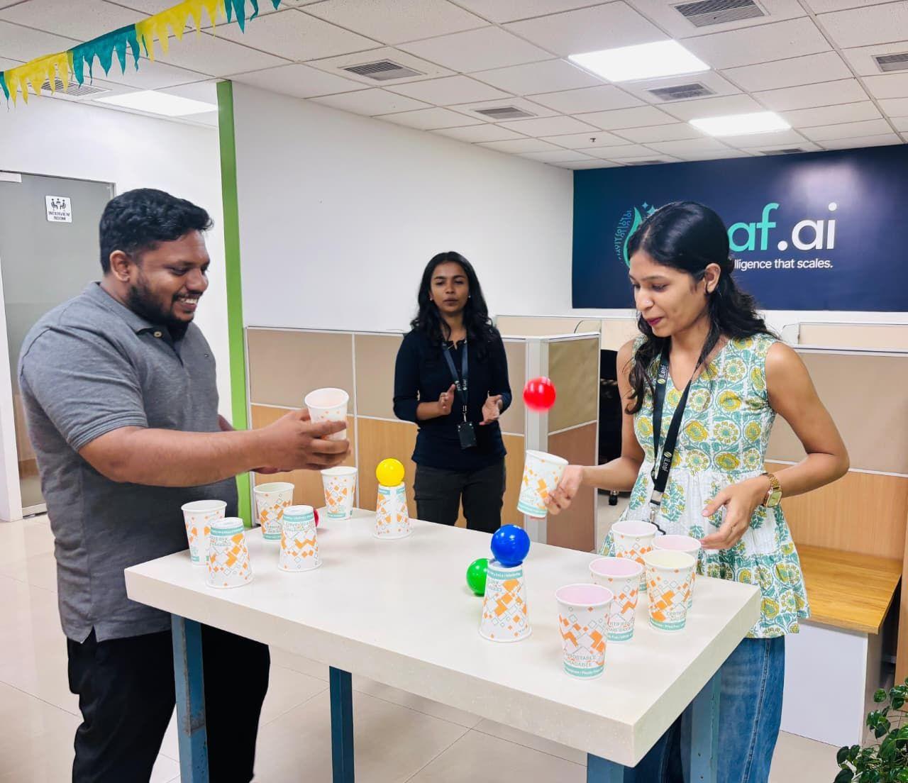 Two iLeaf colleagues playing an office game beneath the ileaf.ai wall sign